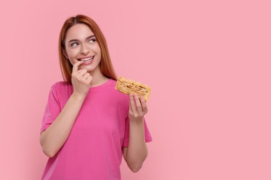Young woman with piece of tasty cake on pink background, space for text
