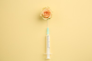 Medical syringe and beautiful rose on pale yellow background, top view