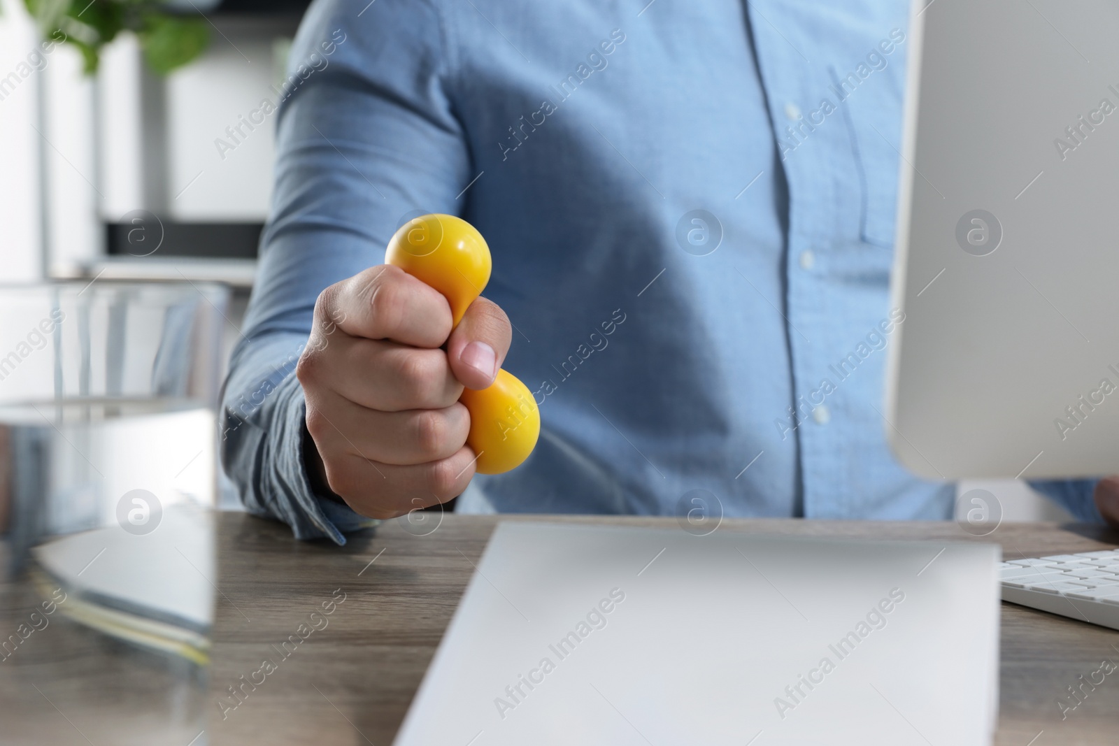 Photo of Man squeezing antistress ball while working with computer in office, closeup