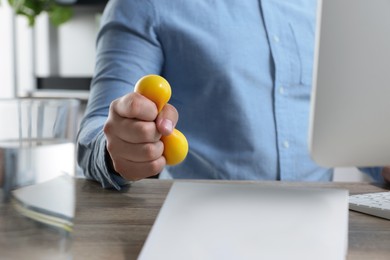 Man squeezing antistress ball while working with computer in office, closeup