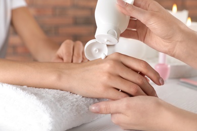 Cosmetologist applying cream on woman's hand at table in spa salon, closeup