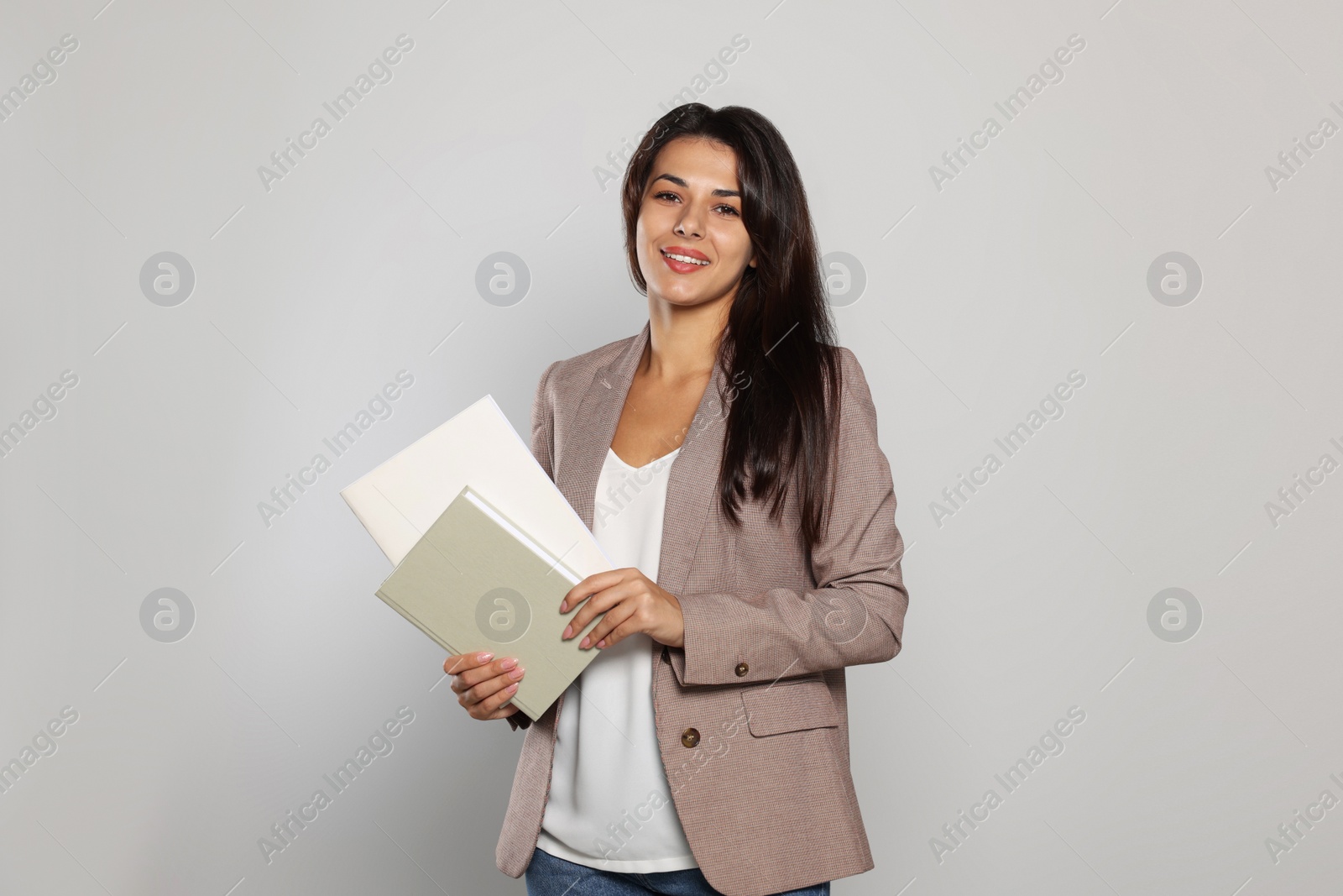 Photo of Happy young teacher with books on light grey background