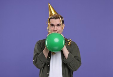 Young man with party hat and balloon on purple background