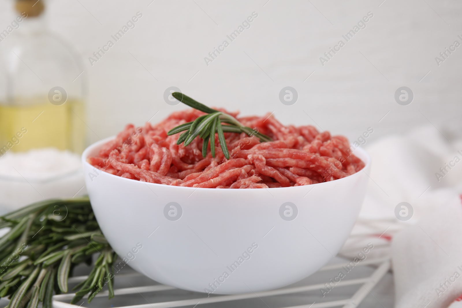 Photo of Fresh raw ground meat and rosemary in bowl on table, closeup
