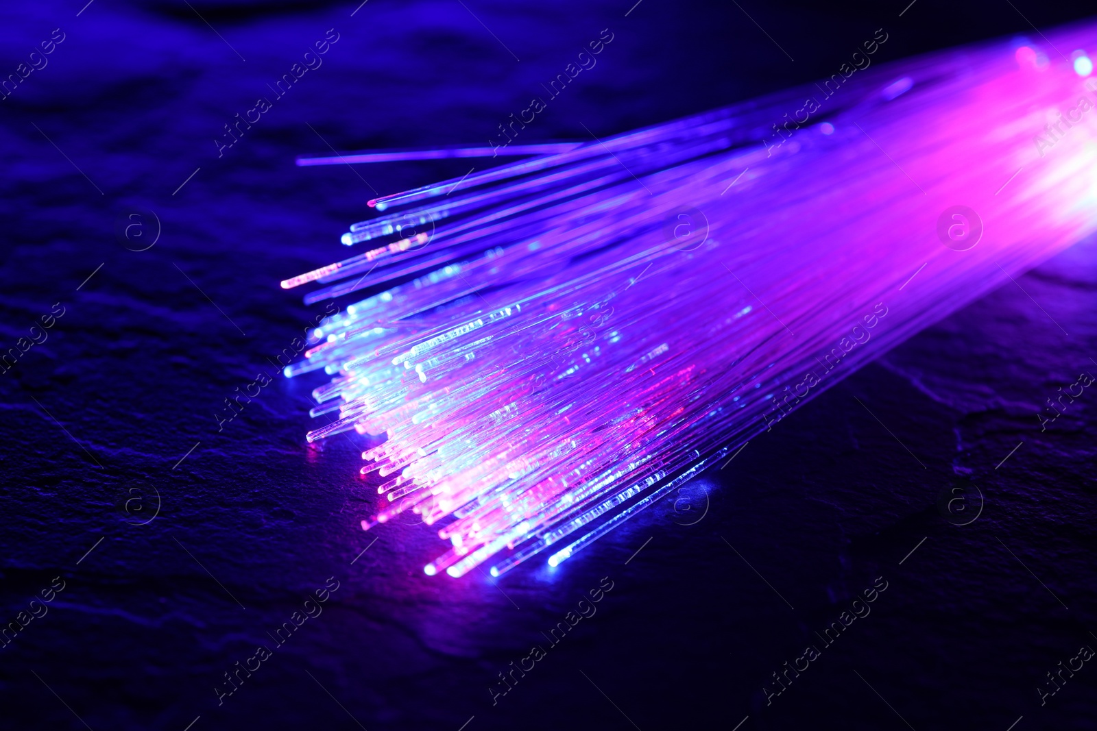 Photo of Optical fiber strands transmitting different color lights on textured background, closeup