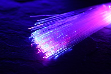 Photo of Optical fiber strands transmitting different color lights on textured background, closeup