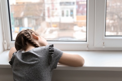 Photo of Lonely little girl near window indoors. Child autism