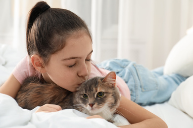 Cute little girl with cat lying on bed at home. First pet