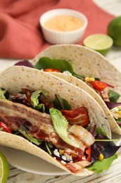 Photo of Delicious tacos with fried bacon on white wooden table, closeup