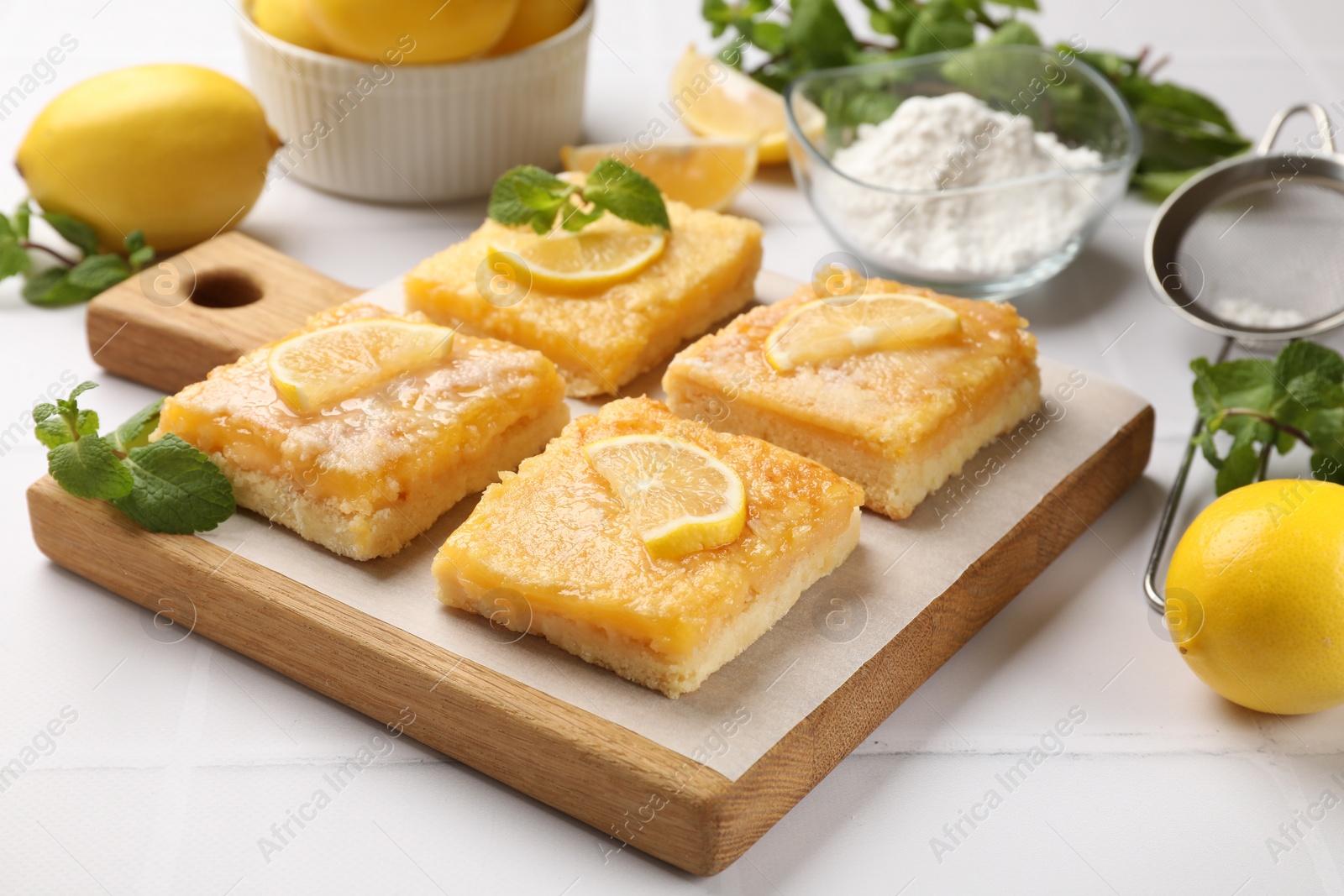 Photo of Tasty lemon bars and mint on white tiled table