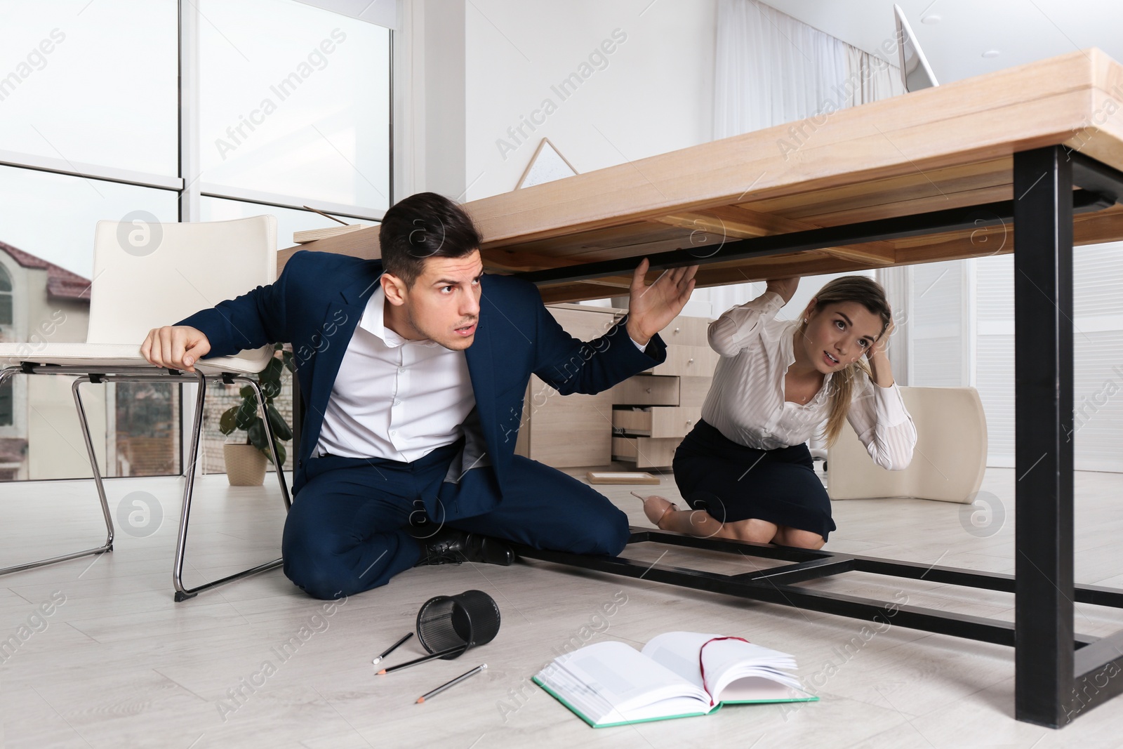 Photo of Scared employees hiding under office desk during earthquake