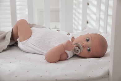 Photo of Cute little baby with pacifier lying on bed