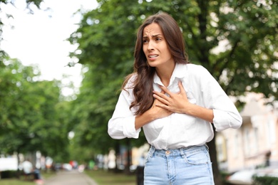 Young woman having heart attack on city street. Space for text