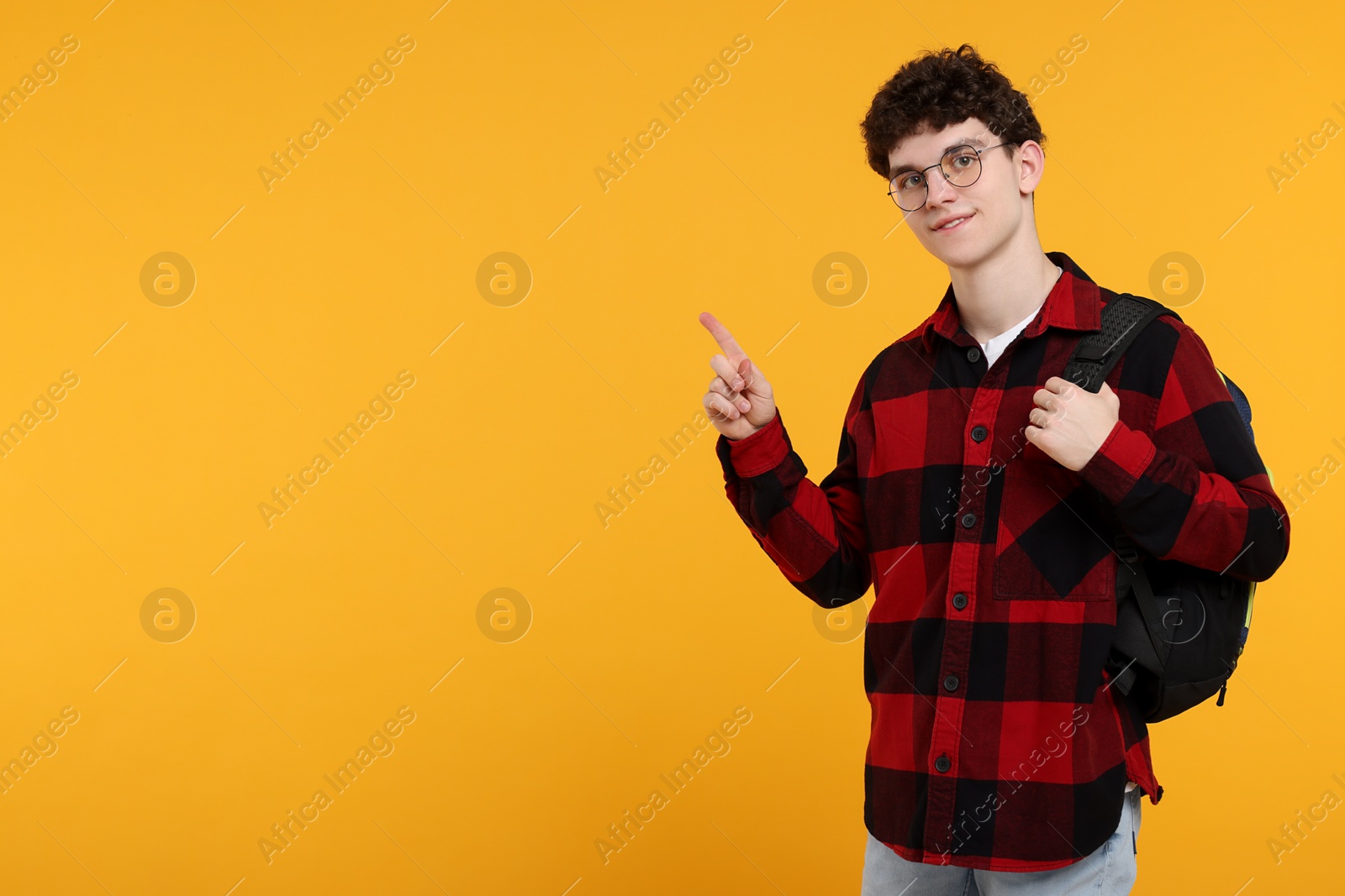 Photo of Portrait of student with backpack pointing on orange background. Space for text