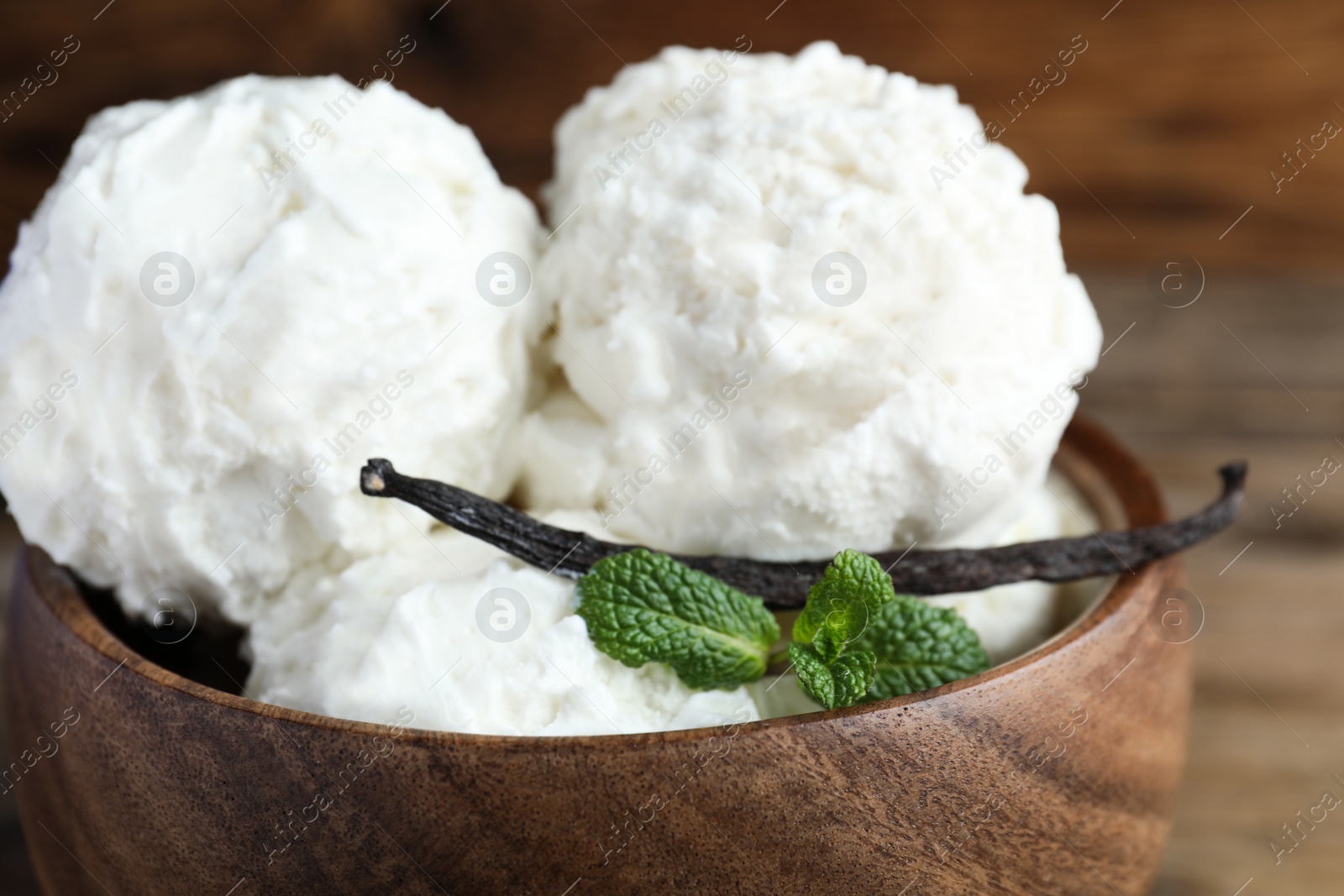 Photo of Yummy vanilla ice cream in wooden bowl, closeup