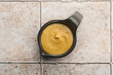 Photo of Tasty mustard sauce in saucepan on light tiled table, top view