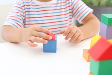 Little boy playing with colorful blocks at white table, closeup. Educational toy