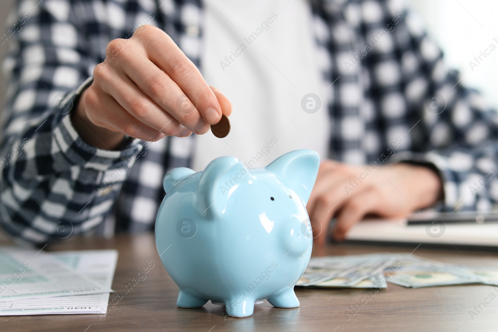 Photo of Financial savings. Man putting coin into piggy bank at wooden table, closeup