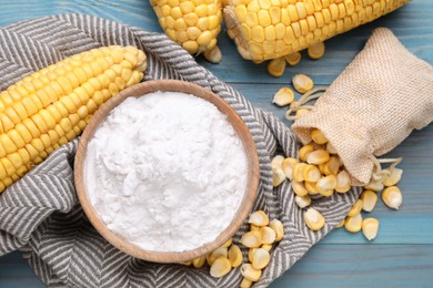 Photo of Bowl with corn starch, ripe cobs and kernels on light blue wooden table, flat lay