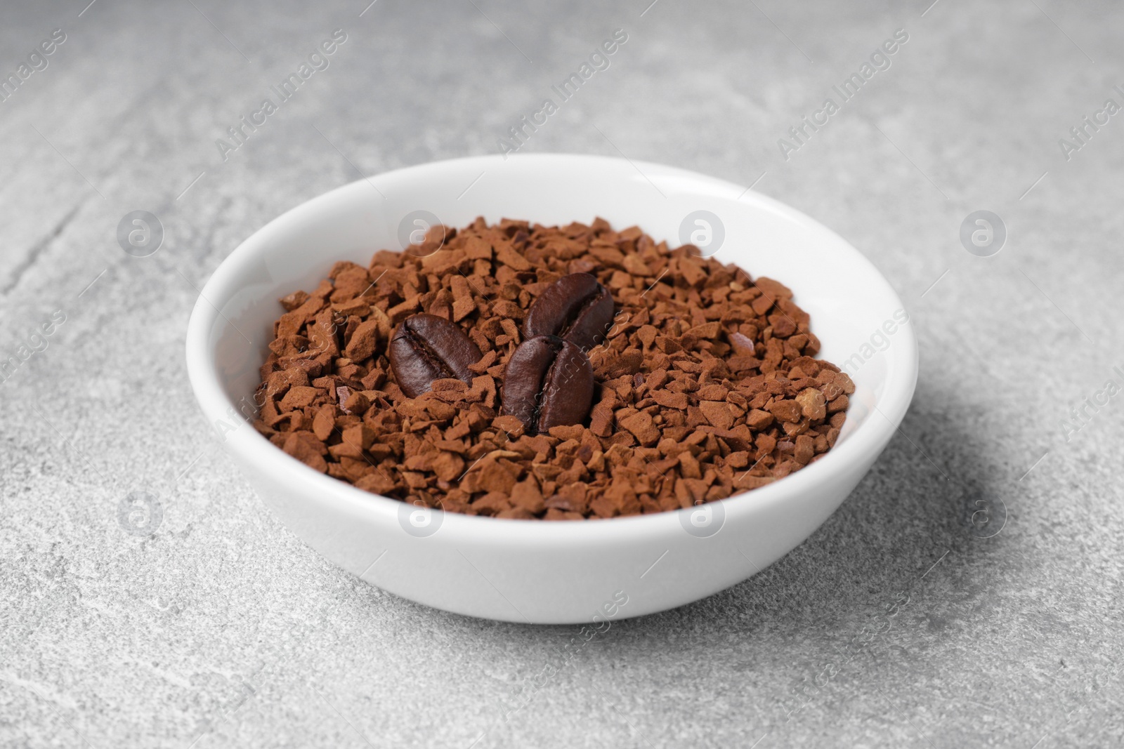 Photo of Bowl with instant coffee and roasted beans on light grey table