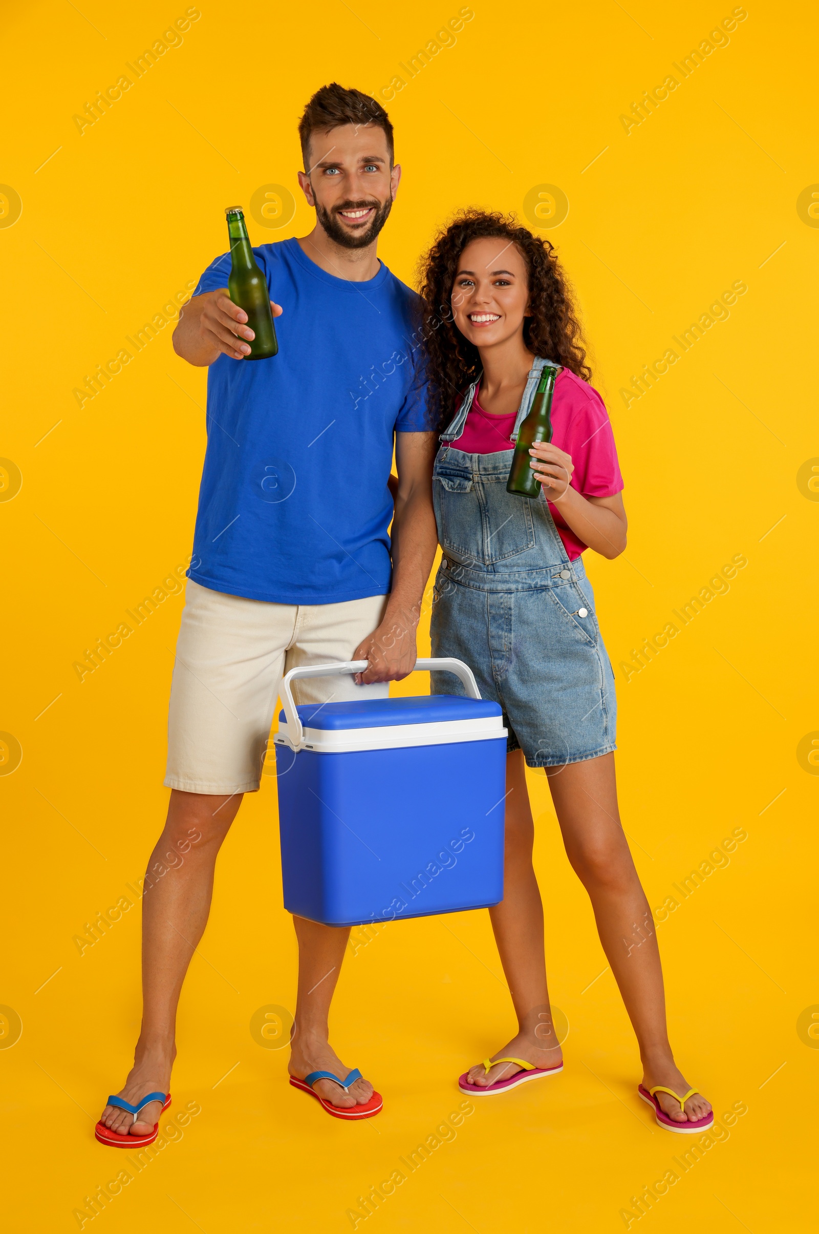 Photo of Happy couple with cool box and bottles of beer on yellow background