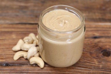 Tasty nut paste in jar and cashews on wooden table, closeup