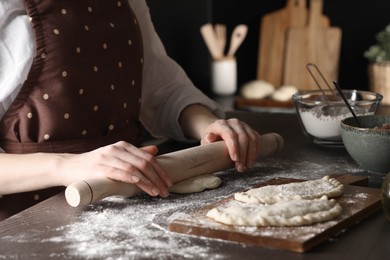 Woman rolling dough for chebureki at wooden table, closeup