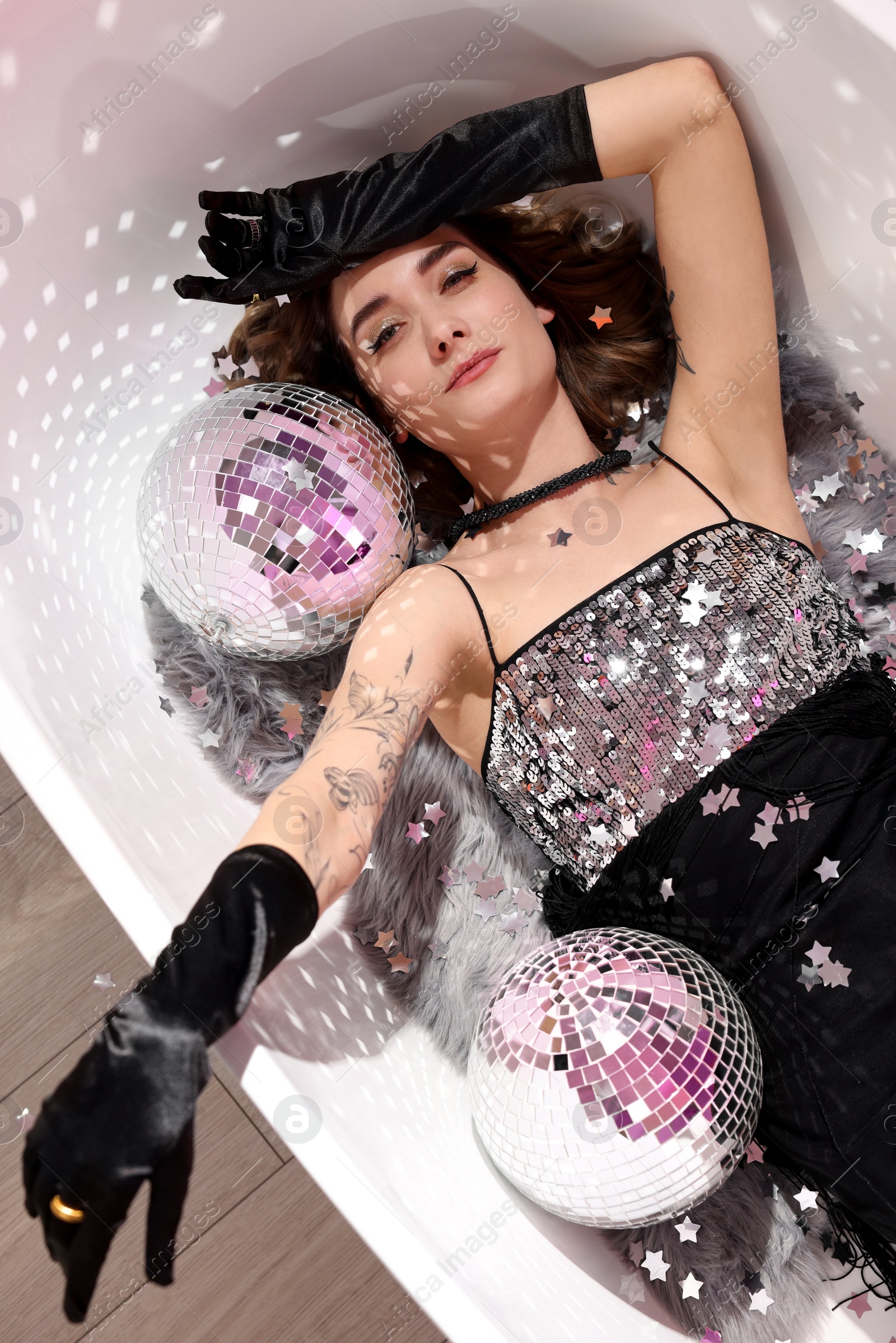 Photo of Beautiful woman in gorgeous dress among disco balls in bathtub, above view