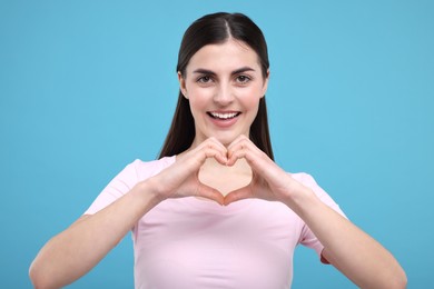 Photo of Beautiful young woman making heart with hands on light blue background