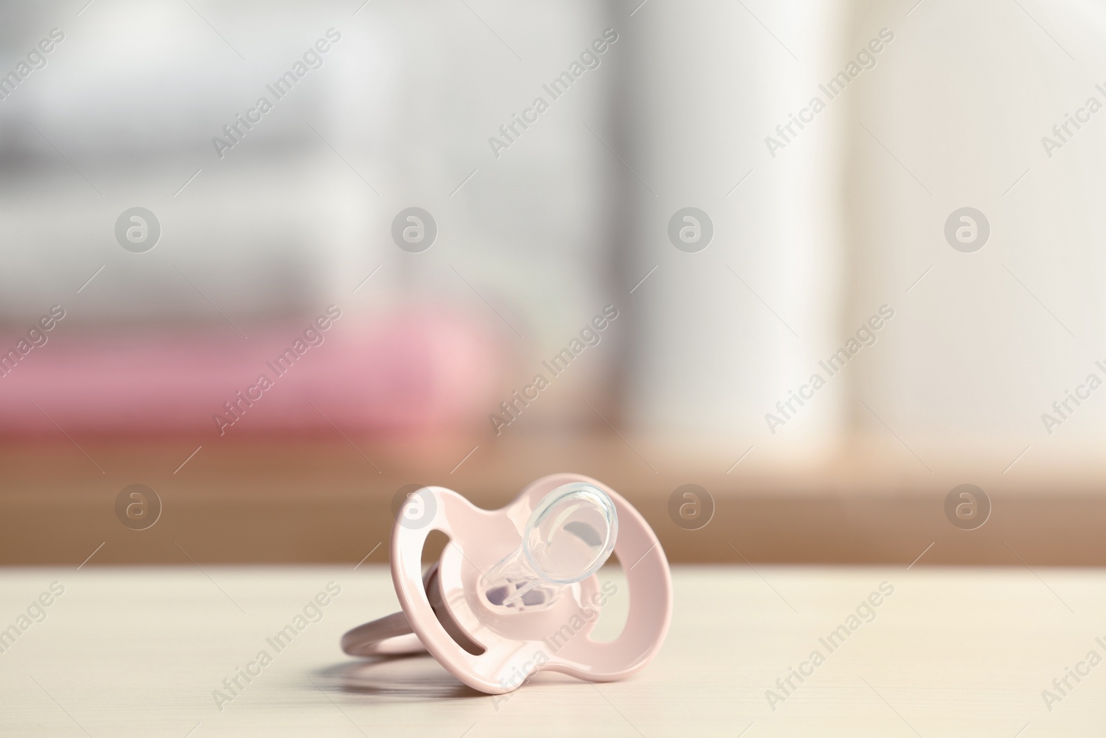 Photo of Baby pacifier on beige table against blurred background, space for text