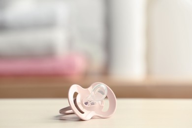 Photo of Baby pacifier on beige table against blurred background, space for text