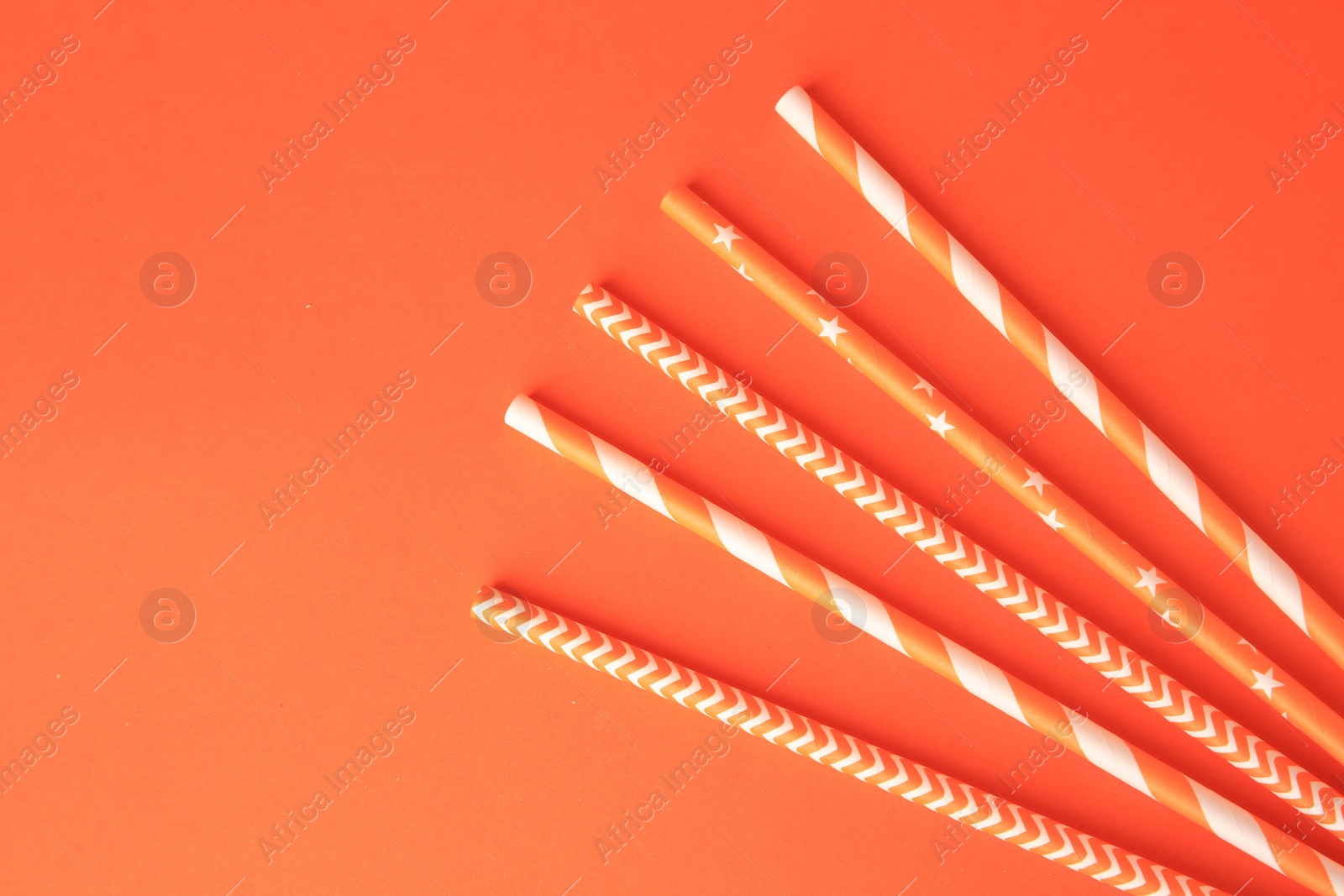Photo of Striped paper drinking straws on orange background, flat lay. Space for text