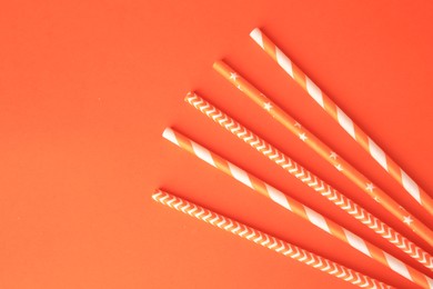 Striped paper drinking straws on orange background, flat lay. Space for text