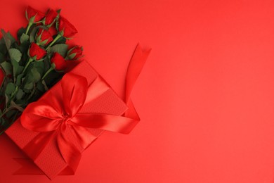 Photo of Beautiful gift box with bow and roses on red background, flat lay. Space for text