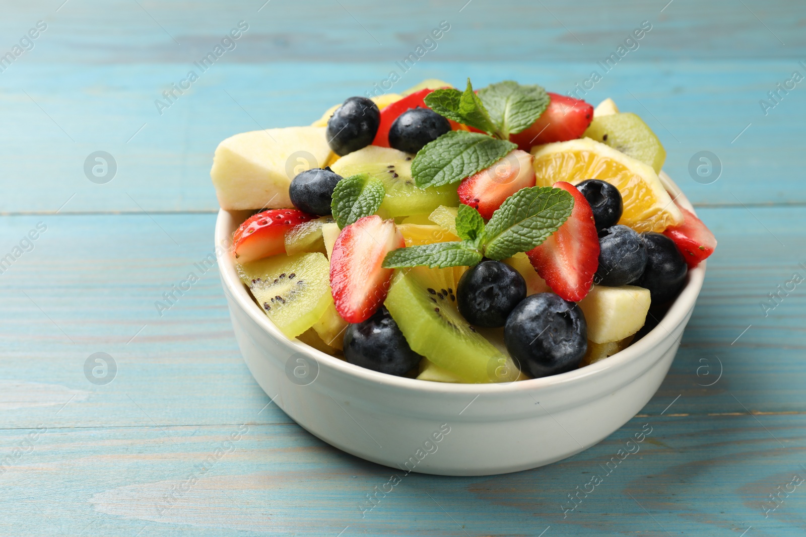 Photo of Tasty fruit salad in bowl on light blue wooden table, closeup. Space for text