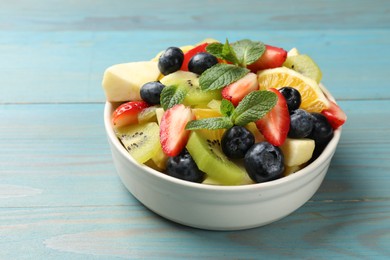 Photo of Tasty fruit salad in bowl on light blue wooden table, closeup. Space for text