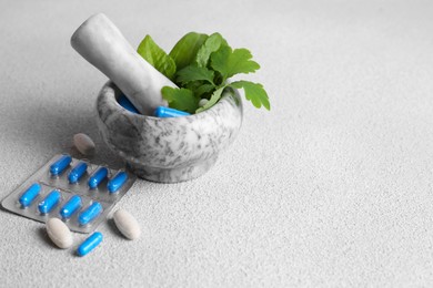 Marble mortar with fresh green herbs and pills on white table, space for text