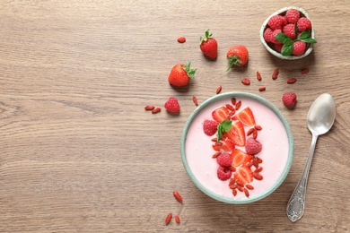 Photo of Smoothie bowl with goji berries and spoon on wooden table, flat lay. Space for text