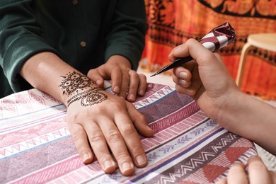 Photo of Master making henna tattoo on hand, closeup. Traditional mehndi