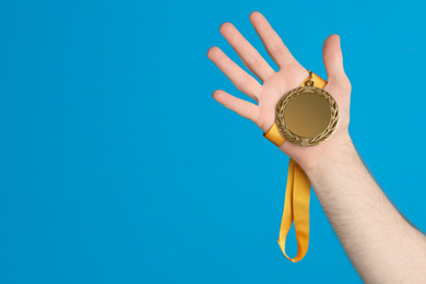 Man holding silver medal on blue background, closeup. Space for design