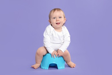 Photo of Little child sitting on baby potty against violet background