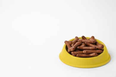 Yellow bowl with bone shaped dog cookies on white background, space for text