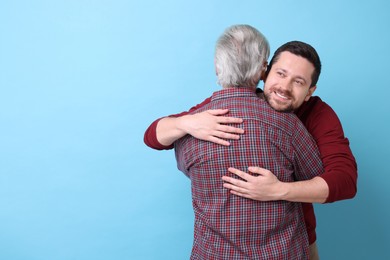 Happy son and his dad hugging on light blue background, space for text