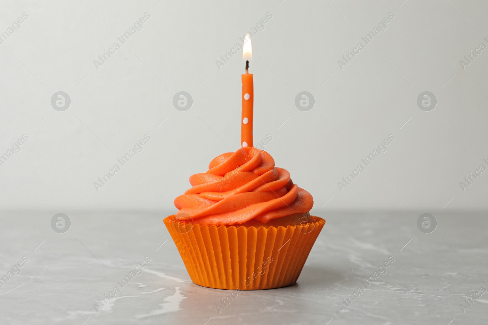 Photo of Delicious birthday cupcake with cream and burning candle on marble table