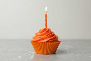 Delicious birthday cupcake with cream and burning candle on marble table