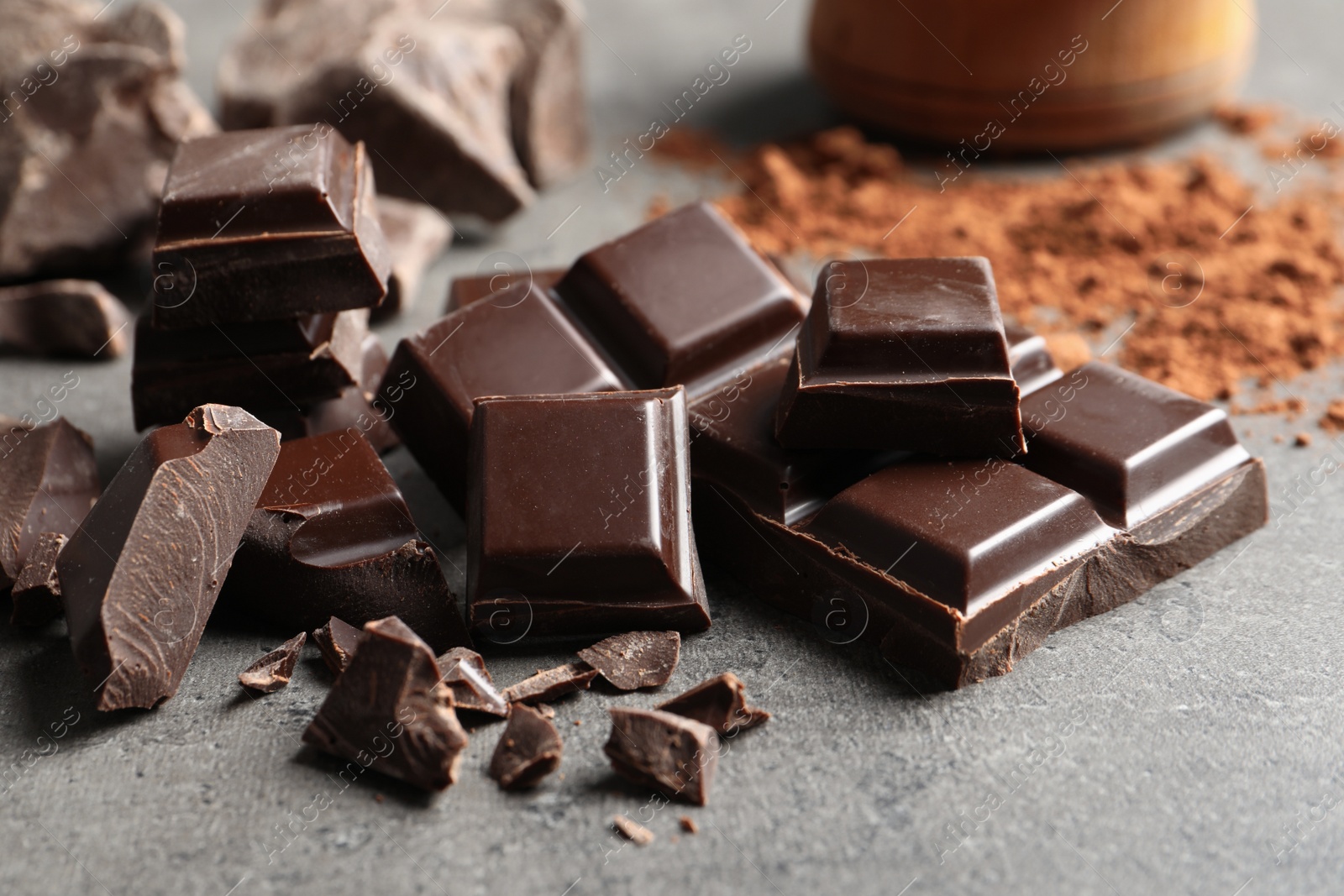 Photo of Pieces of chocolate and cocoa powder on grey background, closeup