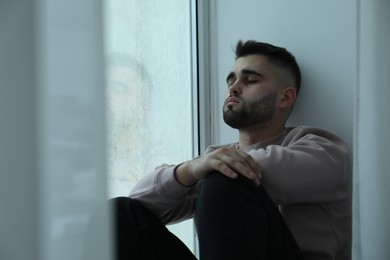 Photo of Sad man sitting near window at home