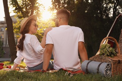 Photo of Lovely couple having picnic on plaid in summer park, back view