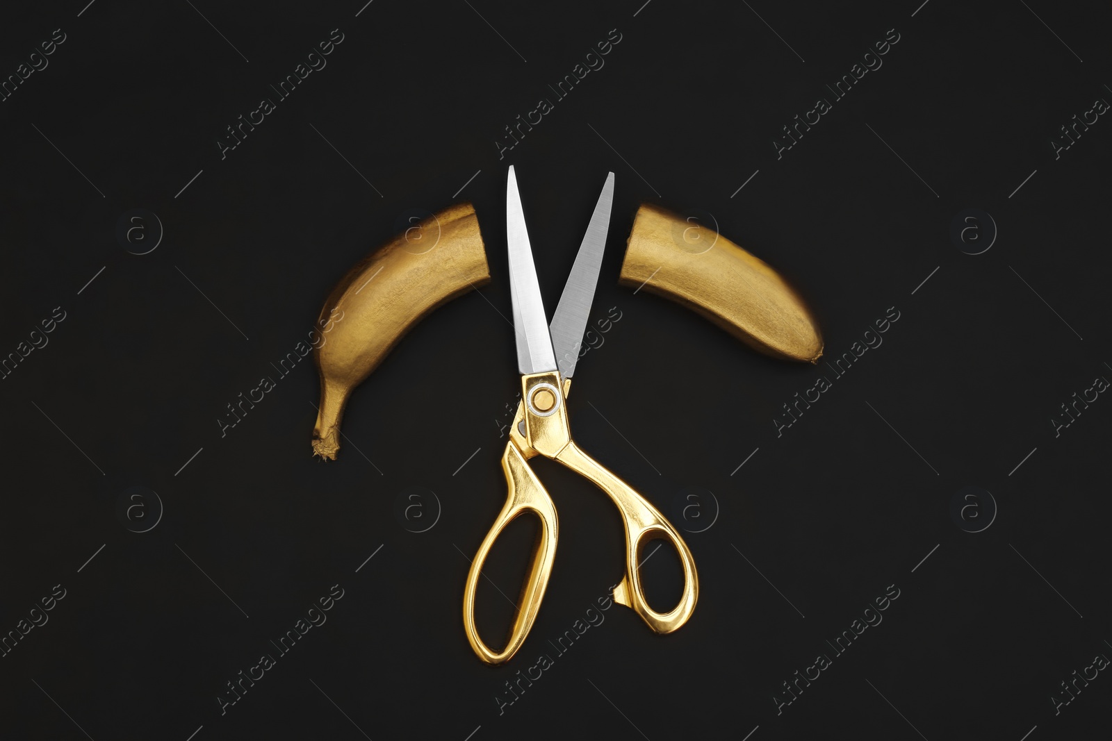 Photo of Gold painted cut banana and scissors on black background, flat lay