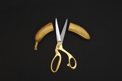 Photo of Gold painted cut banana and scissors on black background, flat lay